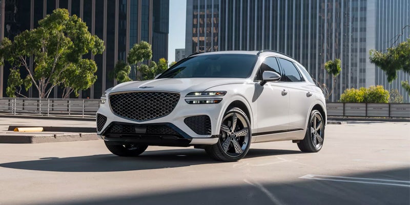 An all-new Alta White 2024 Genesis GV70 parked a top a parking garage in a downtown setting. - Genesis of Baton Rouge, LA