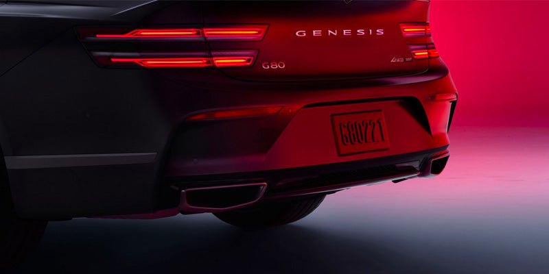 The rear end and tail lights of an all new 2024 Genesis G80 in a photo studio with ambient dark and red lighting. - Genesis of Baton Rouge, LA