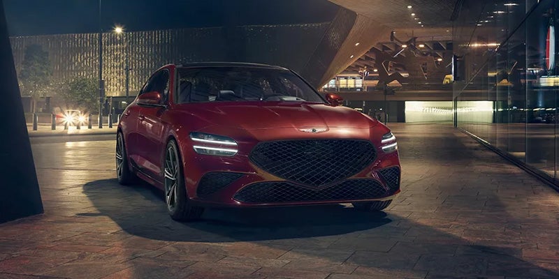 An all new 2024 Red Genesis G70 parked in front of a very modern building. - Genesis of Baton Rouge, LA