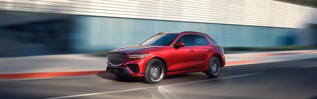 An all-new red 2025 Genesis GV70 cruising on a downtown highway. - Genesis of Baton Rouge, LA