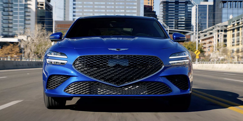 An all-new blue 2025 Genesis G70 driving across a city bridge. - Genesis of Baton Rouge, LA